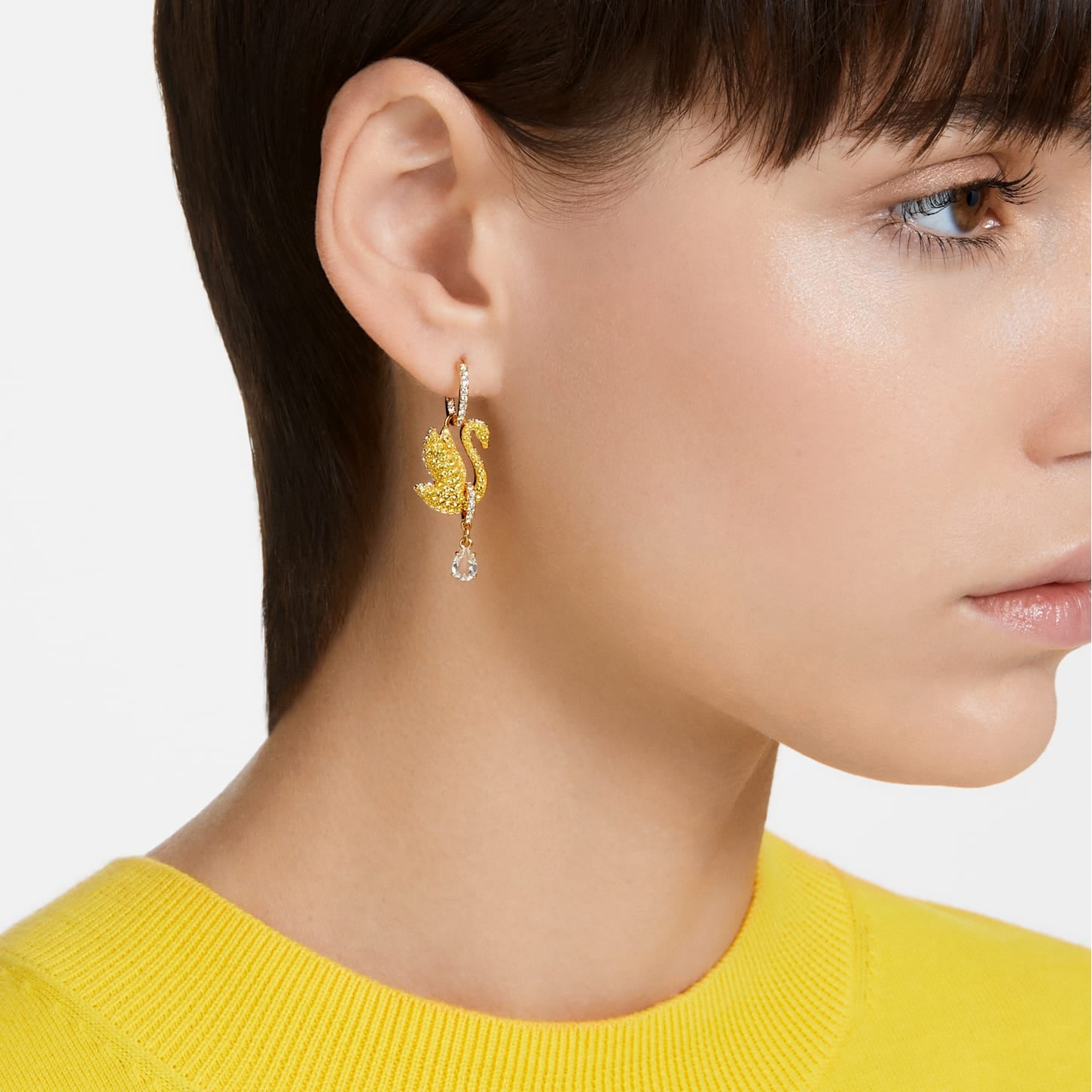 A woman wearing a yellow sweater features Swarovski Iconic Swan drop earrings in yellow with gold-tone plating.