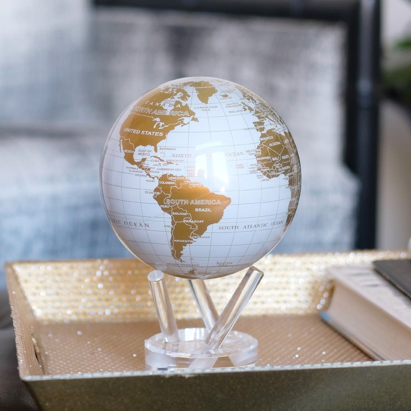 A white and gold MOVA globe with a height of 6 inches, featuring a map with crisp white oceans and gold continents, placed on a clear stand.